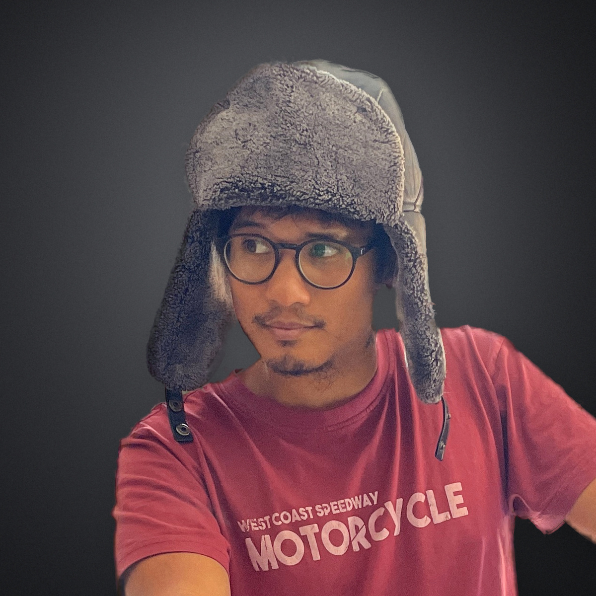 Travis Yangzte studio headshot: fur trapper hat and glasses on a charcoal studio backdrop